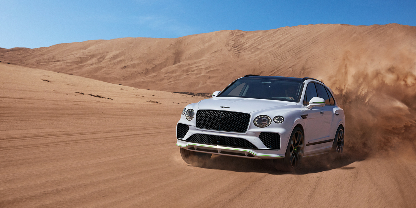 Bentley Leusden Bentley Bentayga Speed SUV front three quarter in Snow Quarts Pearlescent by Mulliner white paint driving dynamically through the desert