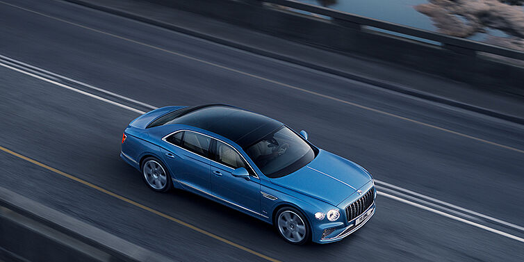 Bentley Leusden New Bentley Flying Spur Azure sedan in Light windsor blue paint by Mulliner, with 22 inch Azure wheels seen from overhead driving dynamically on a country road